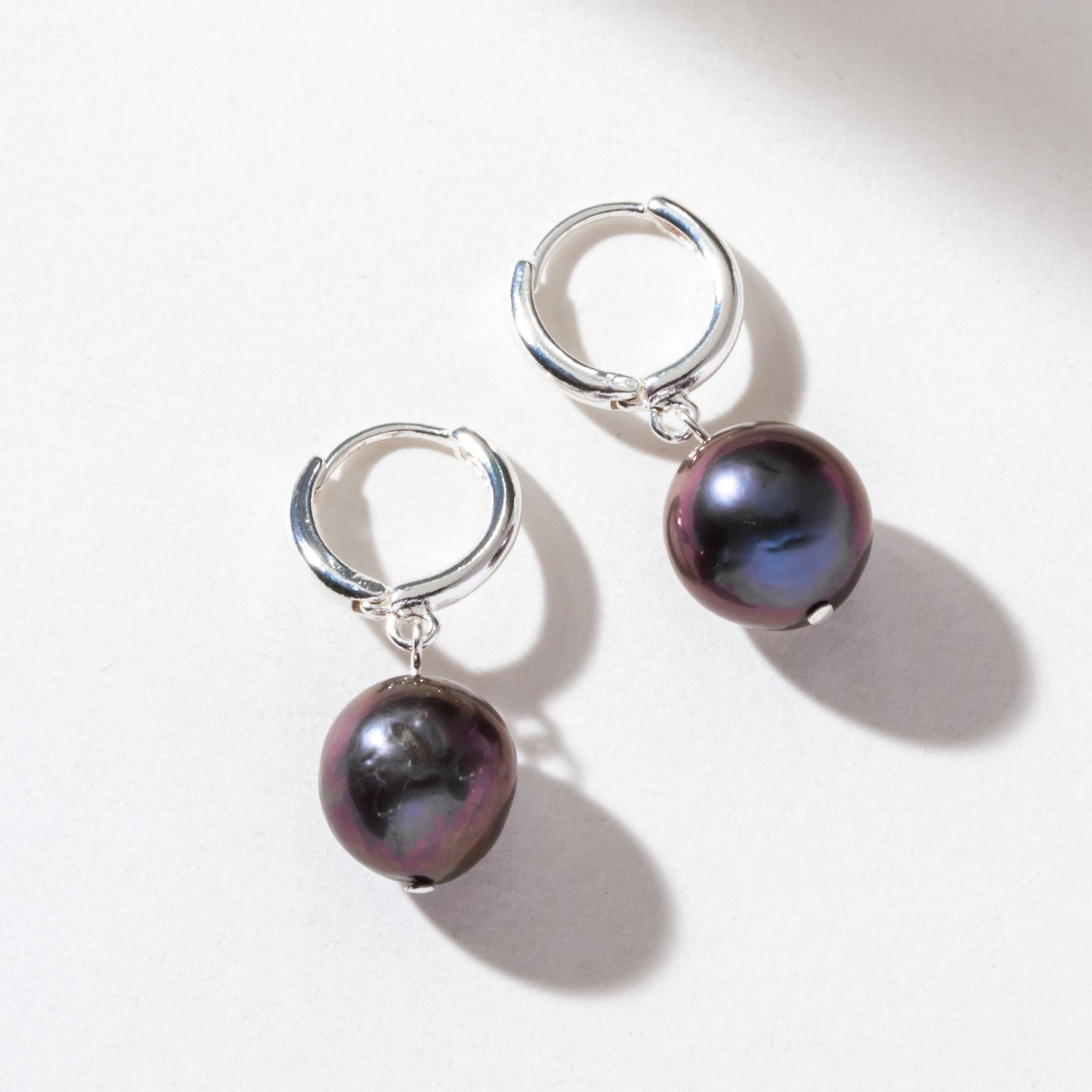 Pair of silver hoop earrings with black pearls on a white background