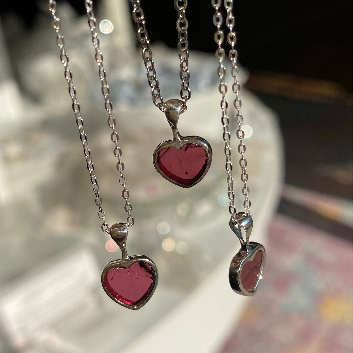 Two heart-shaped pendants on silver chains with a blurred background