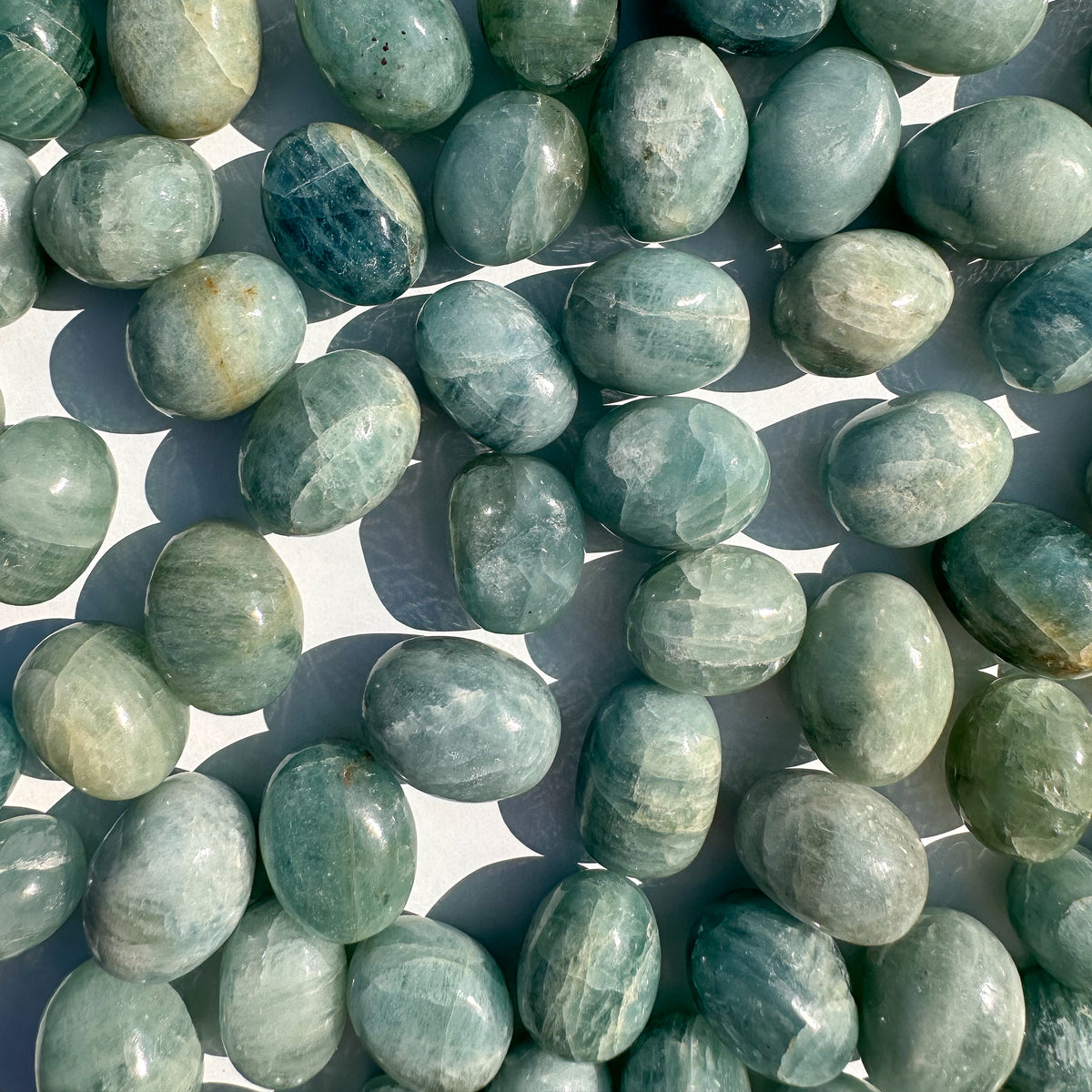 Small-sized, smooth, light blue-ish teal, Aquamarine tumbled pocket stones against a white background.