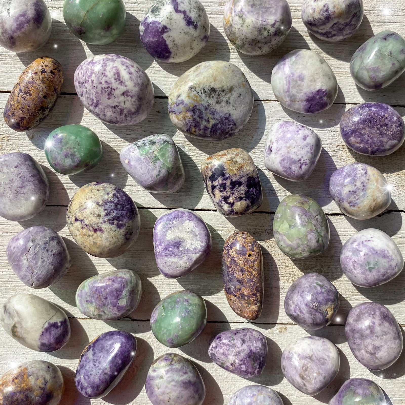 Small-sized, smooth, purple, green, and white, Bolivianite tumbled pocket stones against a wooden background.