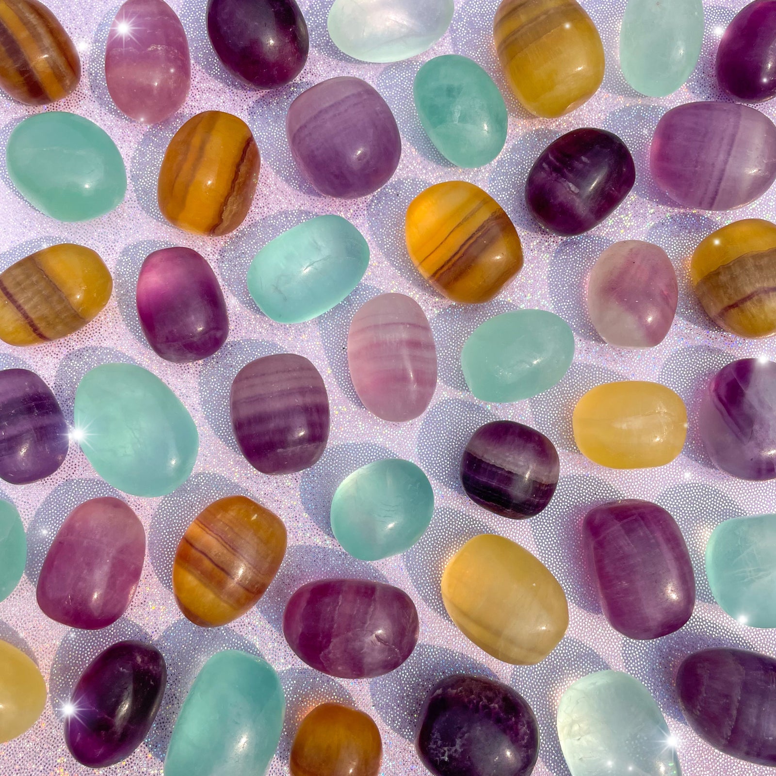 Small-sized, smooth, purple, yellow, and green, gemmy Candy Fluorite tumbled pocket stones against a purple sparkly background.