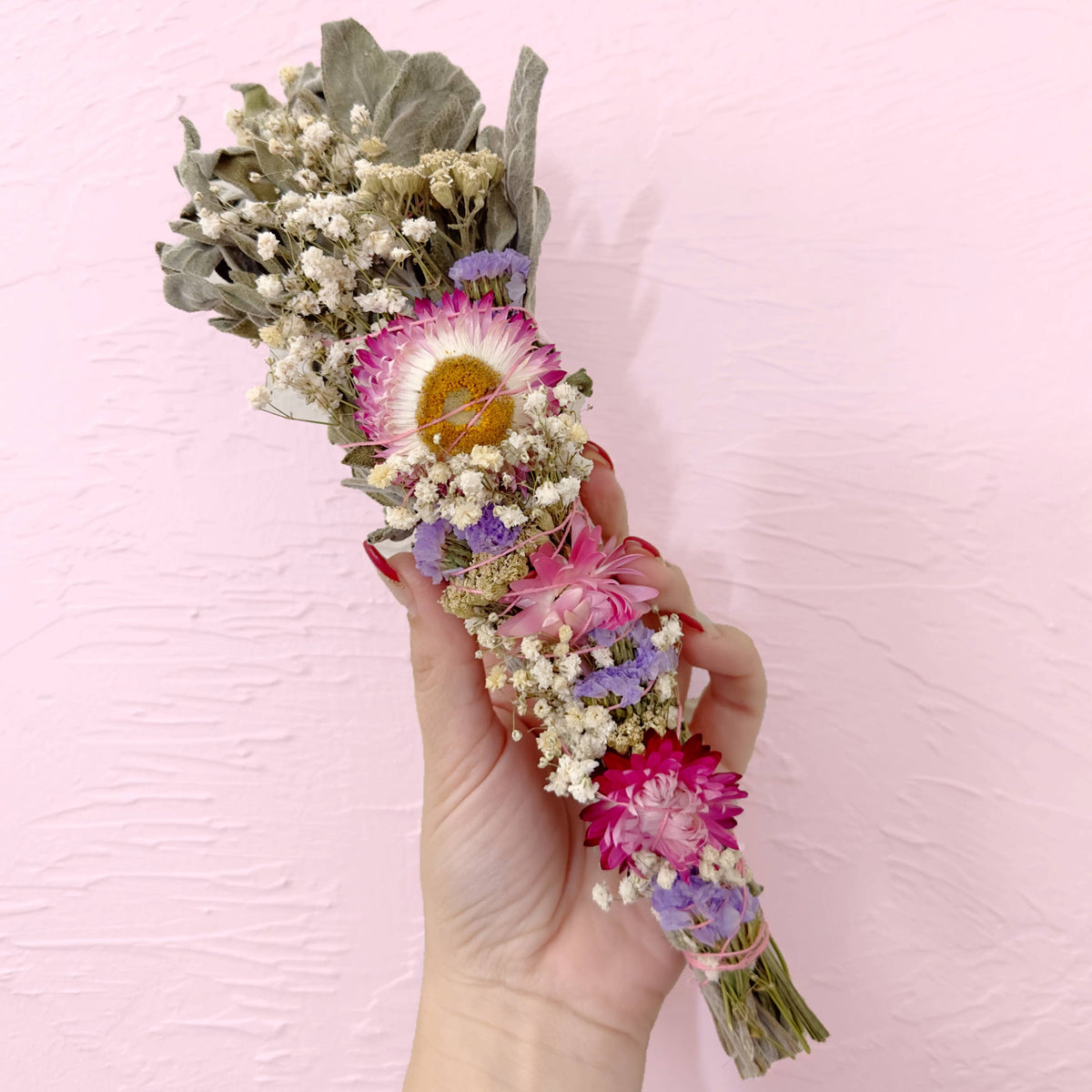 Hand holding a bouquet of dried flowers against a pink background
