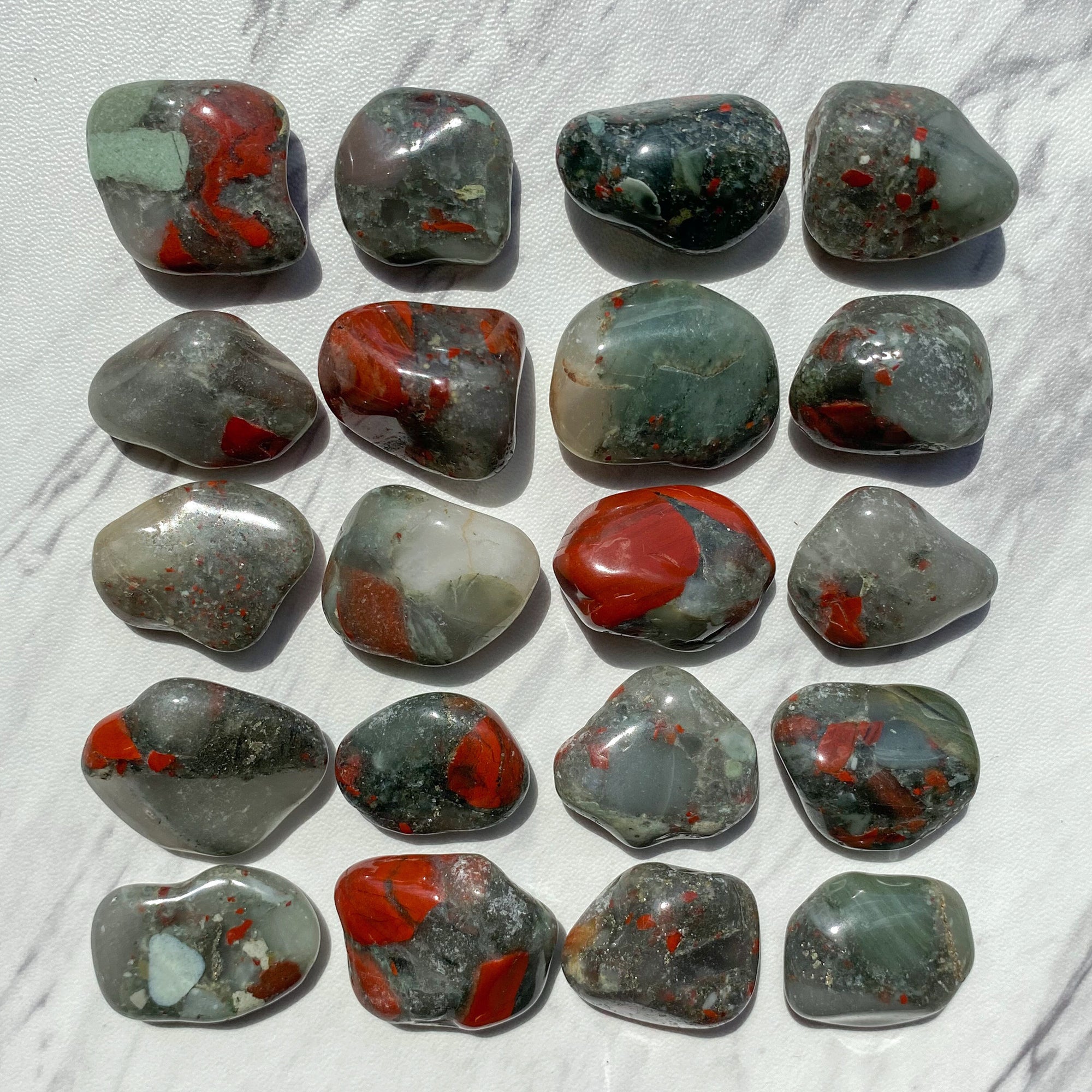 Small-sized, smooth green and red African Bloodstone tumbled pocket stones against marbled background.