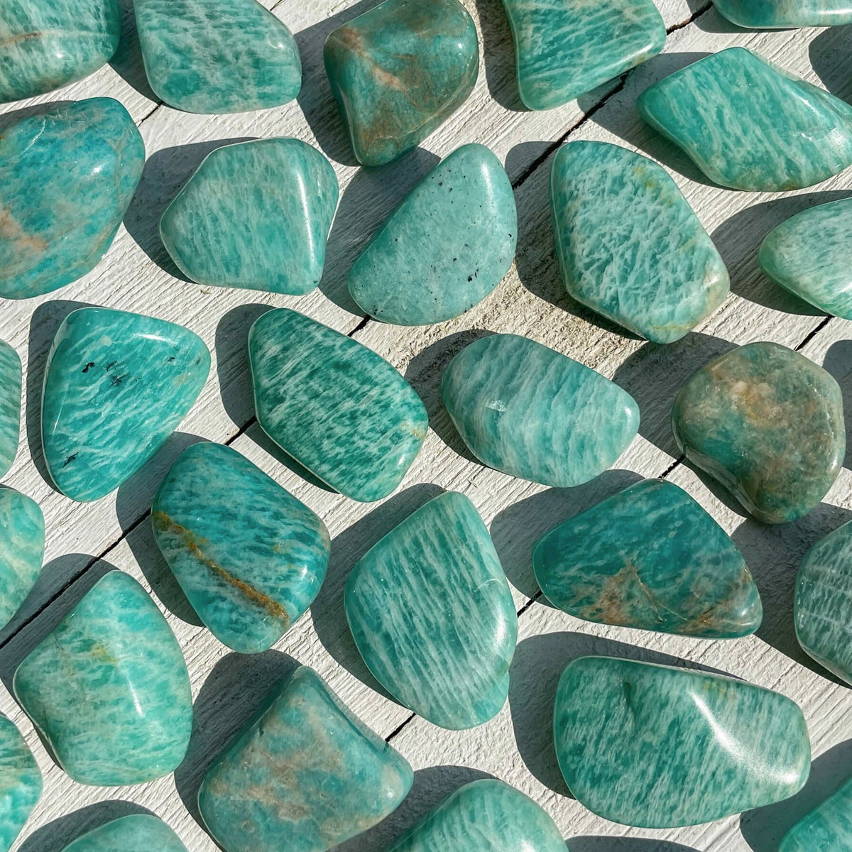 Small-sized, smooth, teal-ish blue Amazonite tumbled pocket stones against a wooden background.