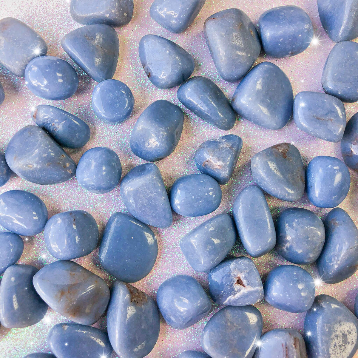 Small-sized, smooth, light blue and white Angelite tumbled pocket stones against a sparkly pink background.