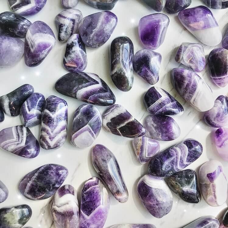 Small-sized, smooth, purple and white striped, Banded Amethyst tumbled pocket stones against a marbled background.