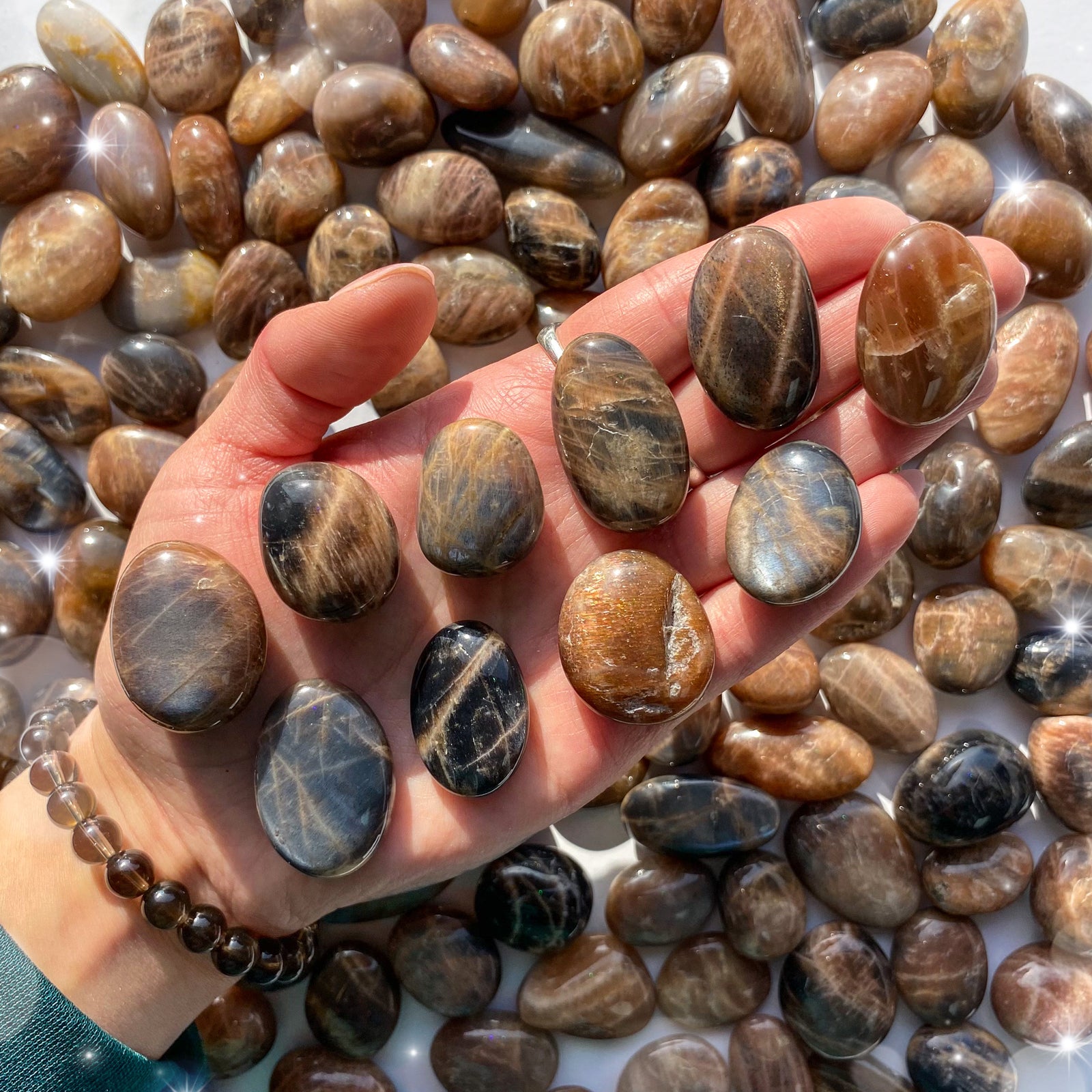 Small-sized, smooth, flashy Black Moonstone and Sunstone tumbled pocket stones being held in a hand.