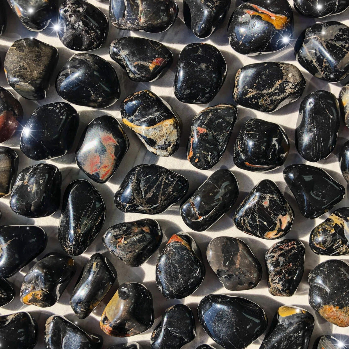 Small-sized, smooth, black, red, and yellow, Black Onyx tumbled pocket stones against a marbled background.