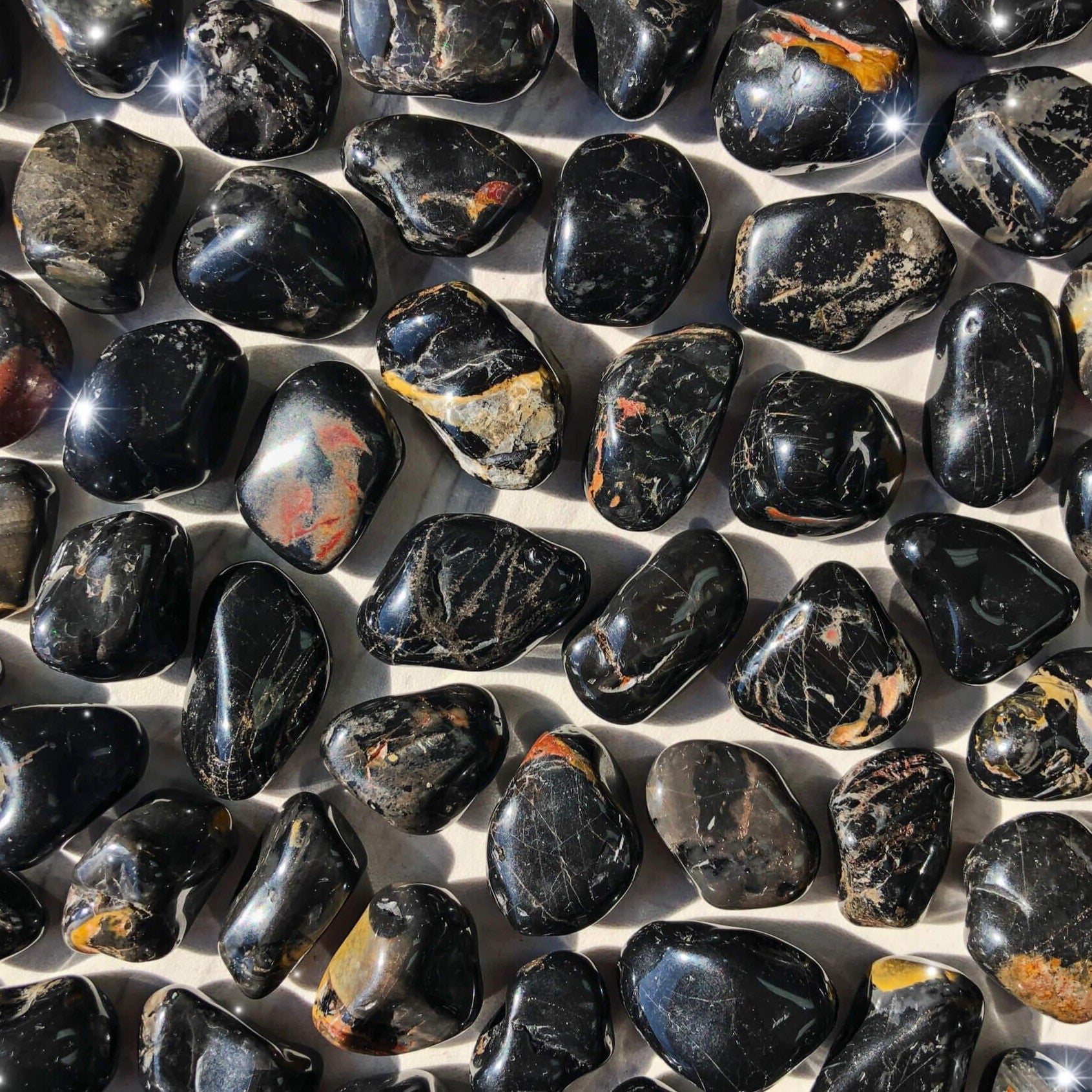 Small-sized, smooth, black, red, and yellow, Black Onyx tumbled pocket stones against a marbled background.