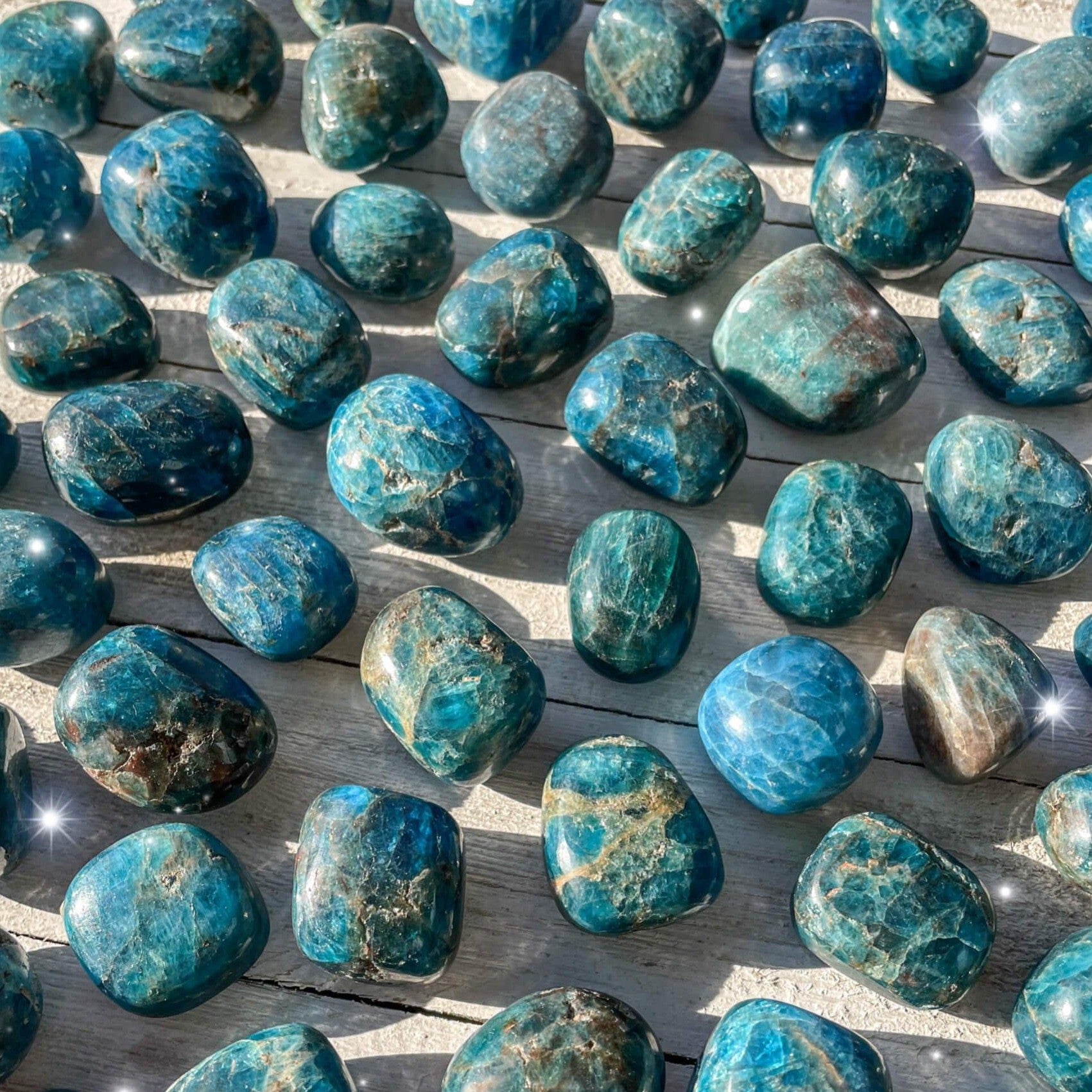 Small-sized, smooth, blue-ish green, Blue Apatite tumbled pocket stones against a wooden background.