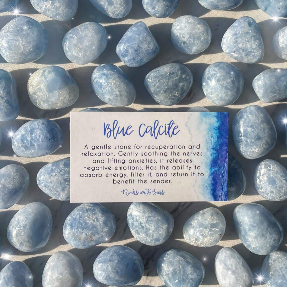 Small-sized, smooth, blue and white, Blue Calcite tumbled pocket stones against a marbled background with a &quot;Blue Calcite&quot; meaning card on top of them.