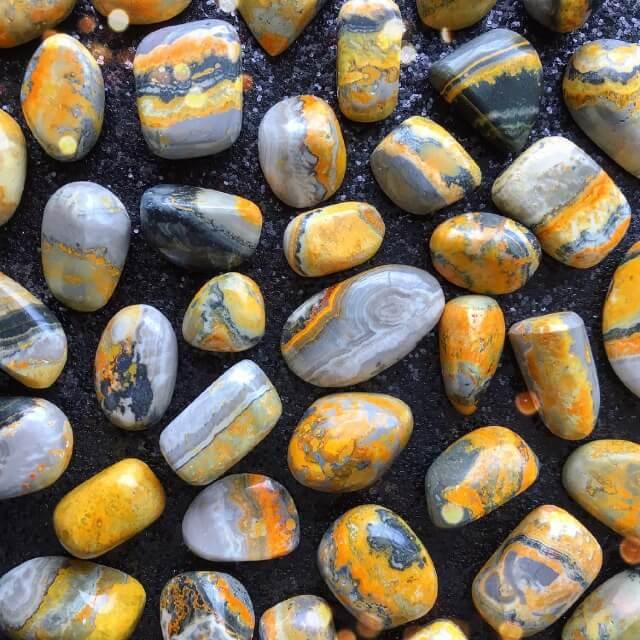 Small-sized, smooth, grey, black, and yellow striped, Bumblebee Jasper tumbled pocket stones against a black glittery background.