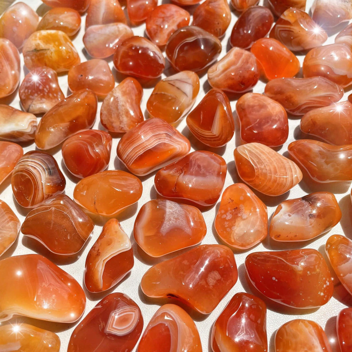 Small-sized, smooth, red, orange, and white banded, Carnelian tumbled pocket stones against a white background.