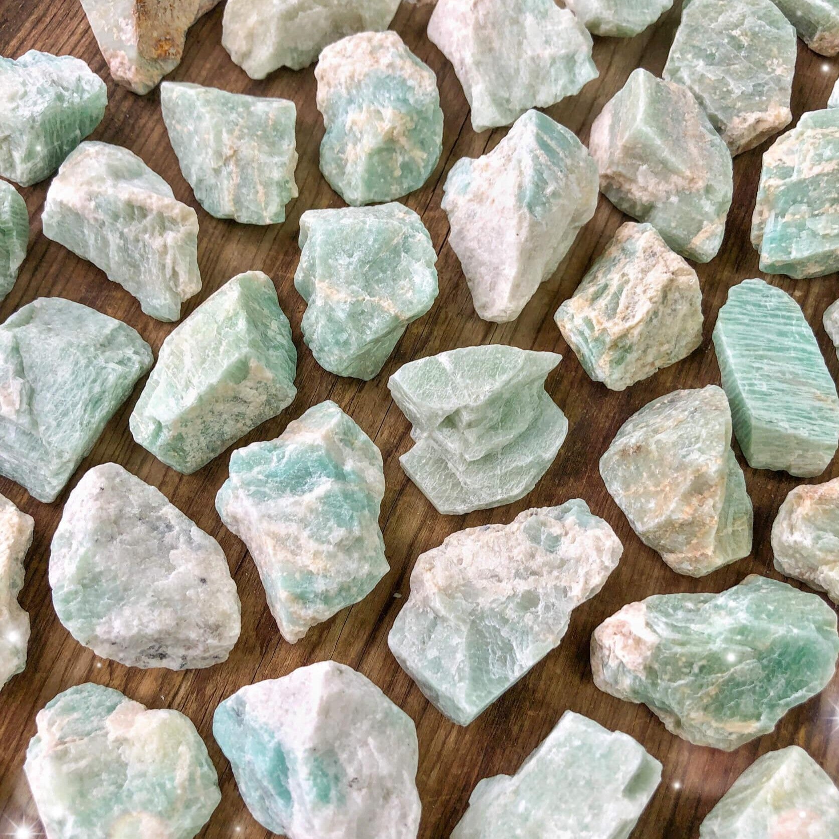 Small-sized, rough, light blue and white raw Amazonite pocket stones against a wooden background.